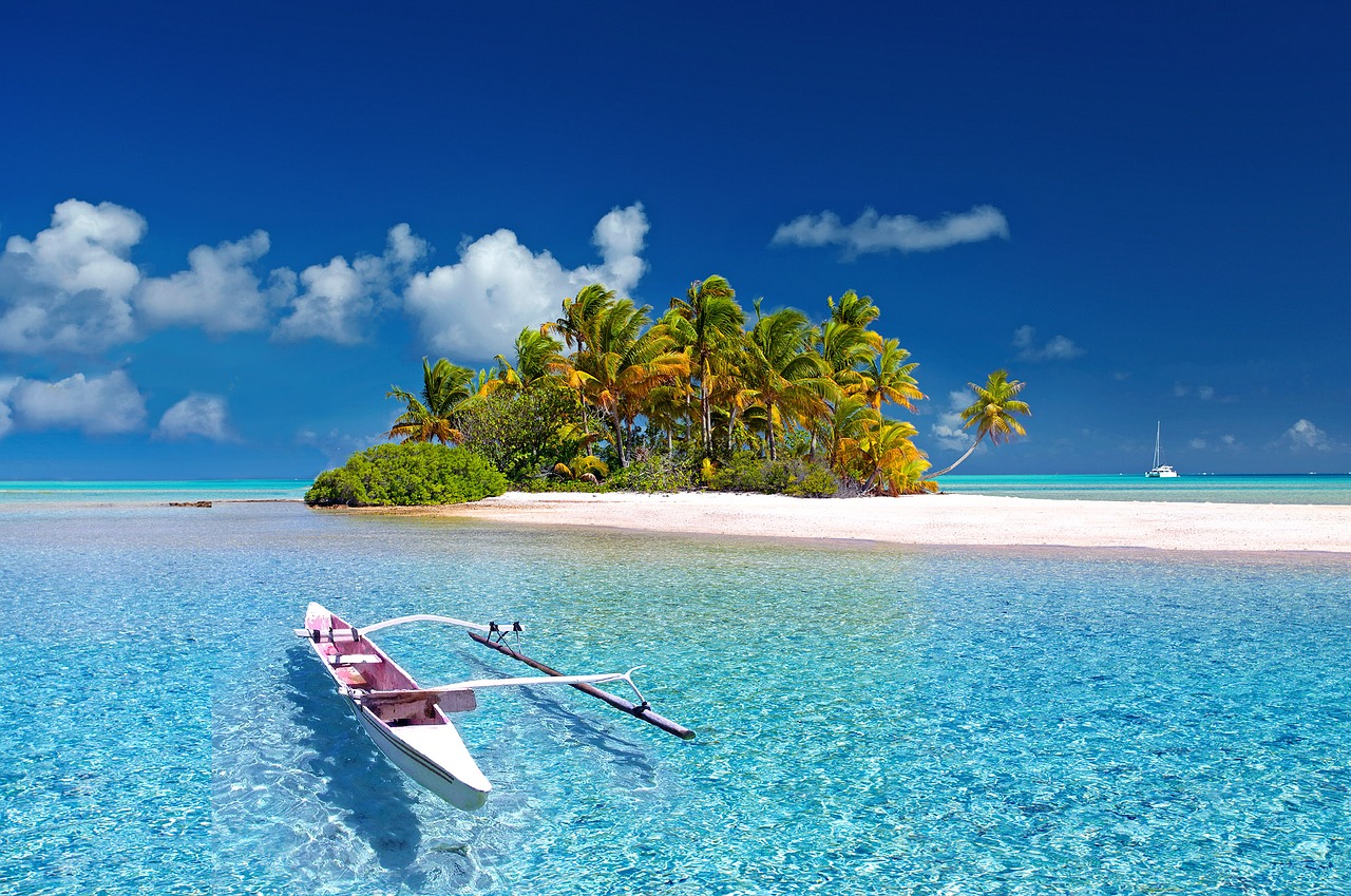 white sand island with coconut trees surrounded with clear water beach with a floating canoe